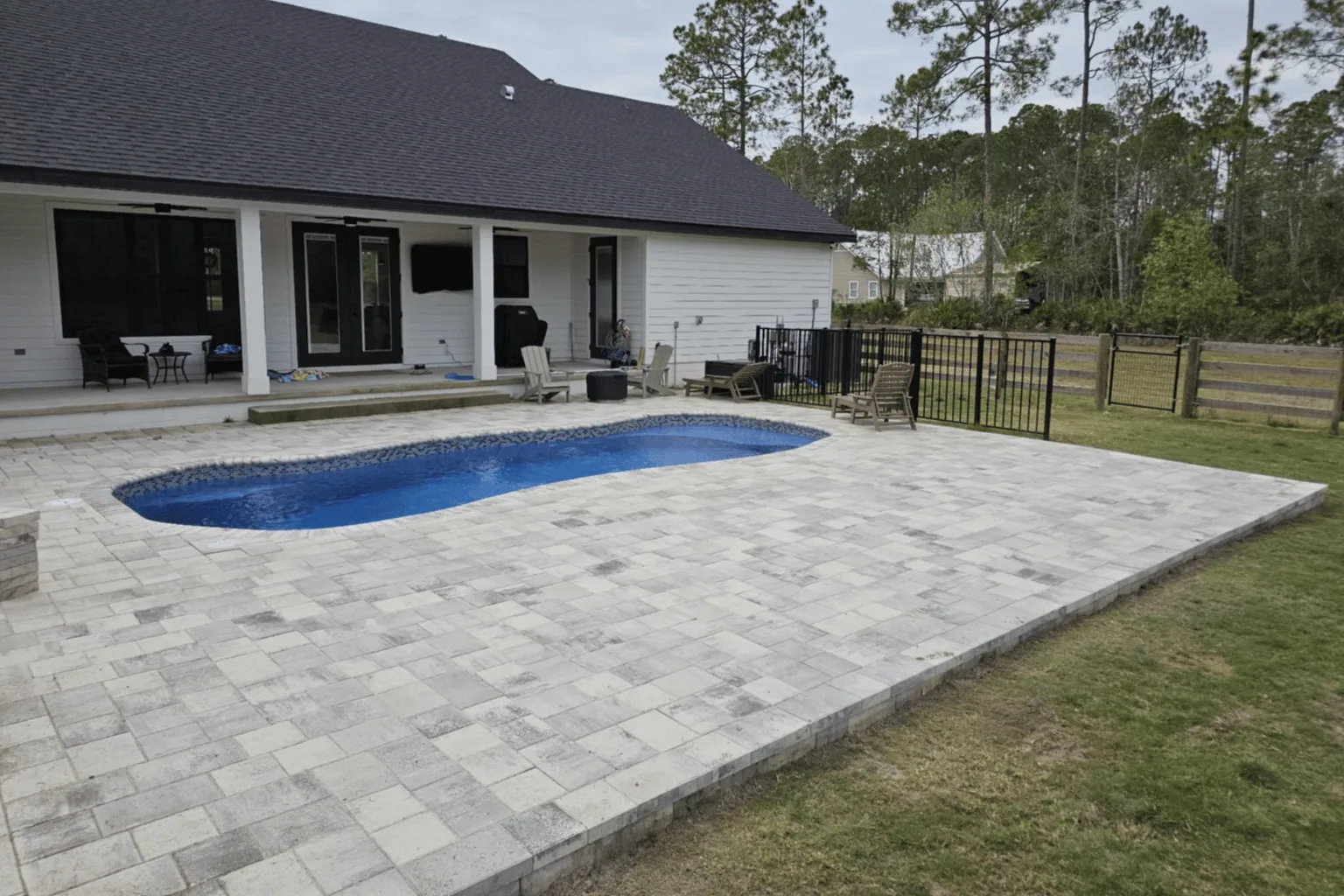 Paver pool deck installation surrounding a freeform pool with covered living area by Jax Pavers in Jacksonville FL
